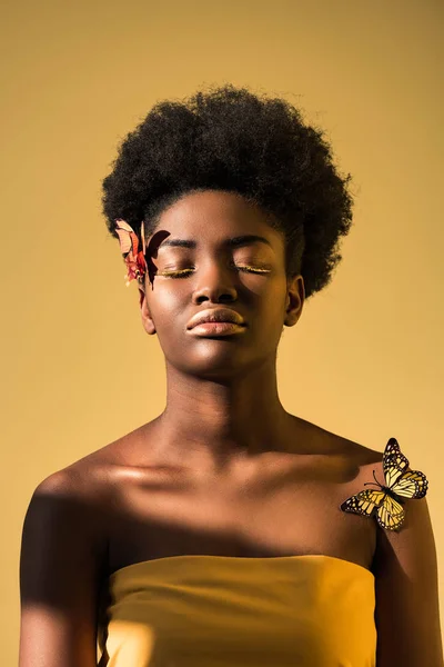 Relajada mujer afroamericana con mariposas con los ojos cerrados aislados en marrón - foto de stock