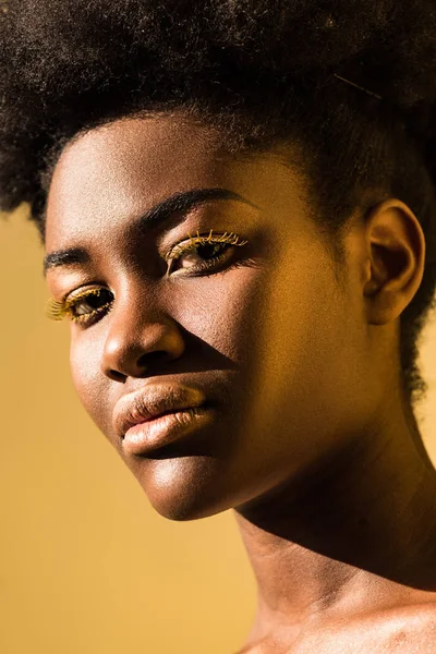 Beautiful african american woman with yellow eyelashes looking at camera isolated on brown — Stock Photo