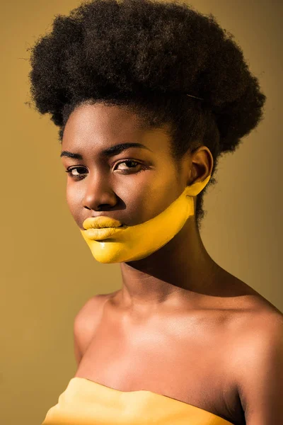 Mujer afroamericana seria con el arte del cuerpo amarillo en marrón - foto de stock