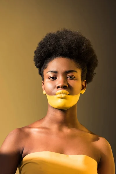 Sérieuse femme afro-américaine au corps jaune art sur brun — Photo de stock