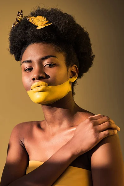Schöne afrikanisch-amerikanische Frau mit Schmetterlingen und gelber Körperkunst auf braun — Stockfoto