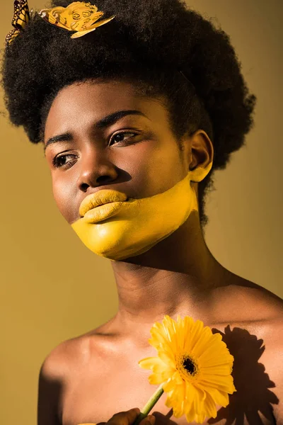 Mujer afroamericana pensativa con mariposas y flor en marrón - foto de stock