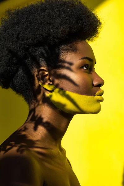 Vue latérale de la femme afro-américaine avec art corporel sur jaune — Photo de stock