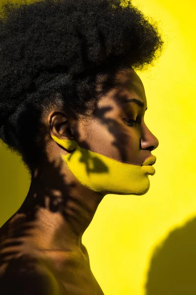 Vista lateral de mujer afroamericana con body art sobre amarillo - foto de stock