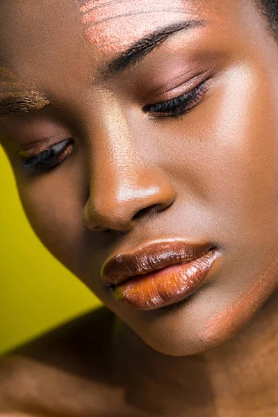Triste hermosa mujer afroamericana con maquillaje mirando hacia abajo en amarillo - foto de stock