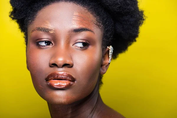 Pensivo attraente donna africana americana con polsino orecchio su giallo — Foto stock