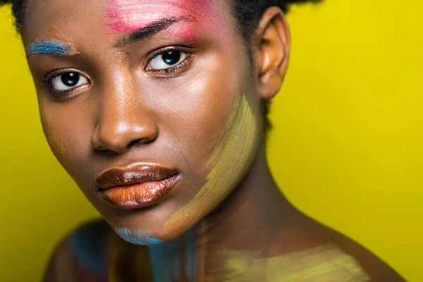 Atractiva mujer afroamericana con maquillaje brillante mirando a la cámara en amarillo - foto de stock