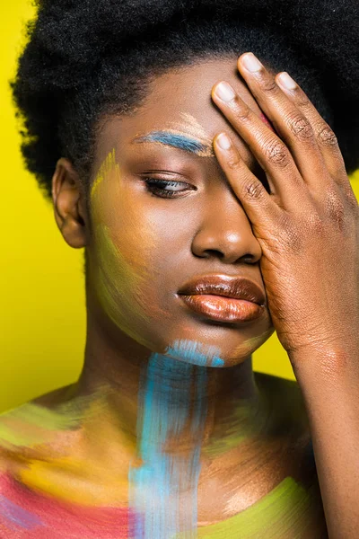 Mujer afroamericana pensativa con cuerpo arte tocando la cara con la mano aislada en amarillo - foto de stock