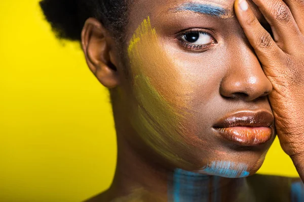 Pensativa mujer afroamericana con cuerpo arte tocando la cara con la mano en amarillo - foto de stock