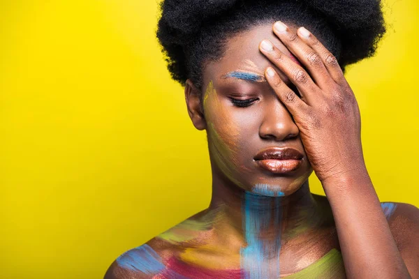 Pensiva donna afroamericana con body art toccare il viso con mano sul giallo — Foto stock