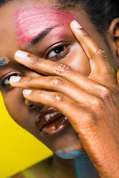 Hermosa mujer africana con cuerpo arte tocando la cara con la mano aislada en amarillo - foto de stock