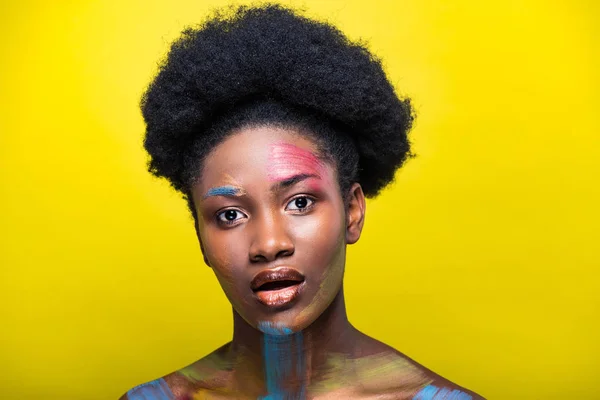 Здивувало афроамериканець дівчина з яскравим макіяж дивлячись на камеру на жовтому — стокове фото