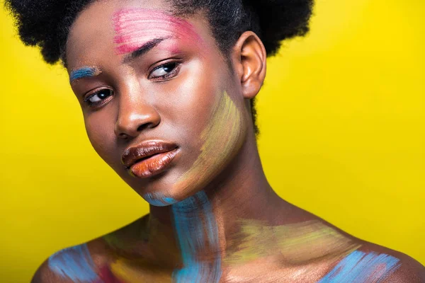 Pensativo africano americana mujer con colorido cuerpo arte en amarillo - foto de stock