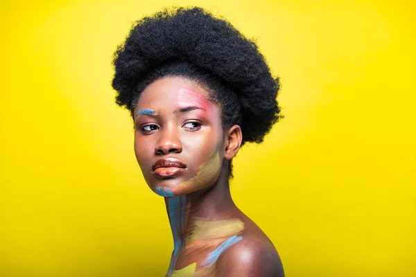 Pensativo africano americana mujer con colorido cuerpo arte en amarillo - foto de stock