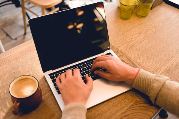 Vista recortada del freelancer utilizando el ordenador portátil con pantalla en blanco cerca de taza con café - foto de stock