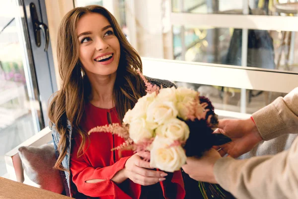 Cropped view of man giving flowers to cheerful girlfriend in cafe — Stock Photo