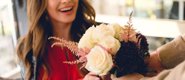 Panoramic shot of man giving flowers to cheerful girlfriend in cafe — Stock Photo