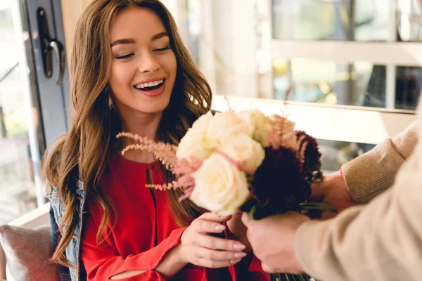 Foco seletivo da menina feliz olhando para as flores nas mãos do namorado — Fotografia de Stock