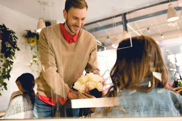 Handsome boyfriend giving flowers to woman in cafe — Stock Photo