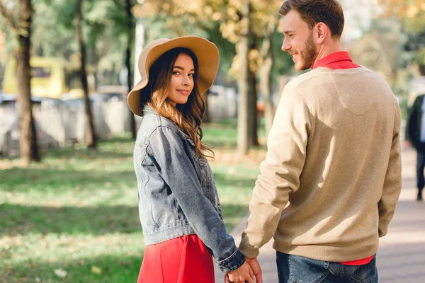 Schöner Mann schaut attraktive Freundin mit Hut an, während er sich im Park an den Händen hält — Stockfoto