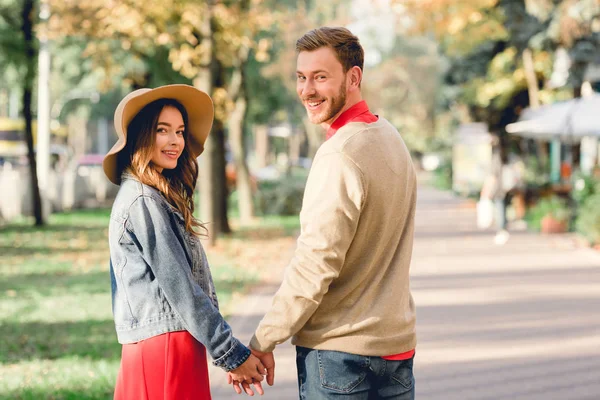 Fidanzato allegro e fidanzata felice in cappello tenendosi per mano e guardando la fotocamera — Foto stock