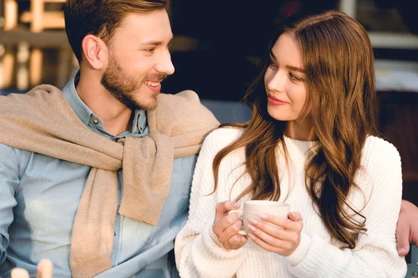 Cheerful boyfriend looking at happy girlfriend holding cup of coffee — Stock Photo