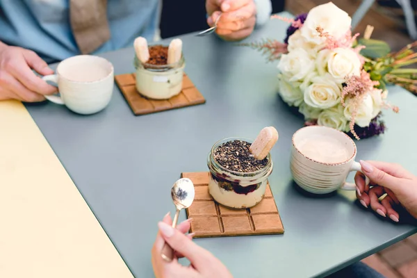 Cropped view of man and woman holding spoons near desserts and cups in cafe — Stock Photo