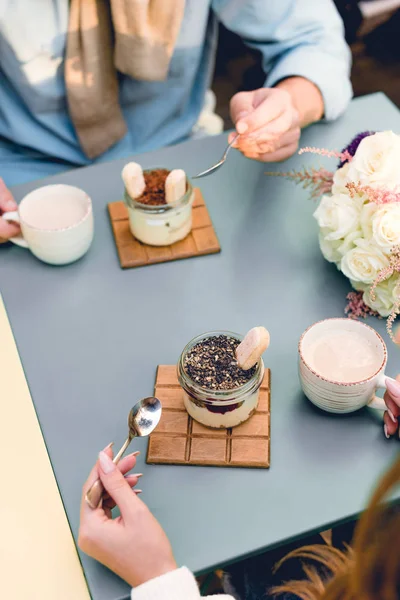 Overhead view of man and woman holding spoons near desserts and cups in cafe — Stock Photo