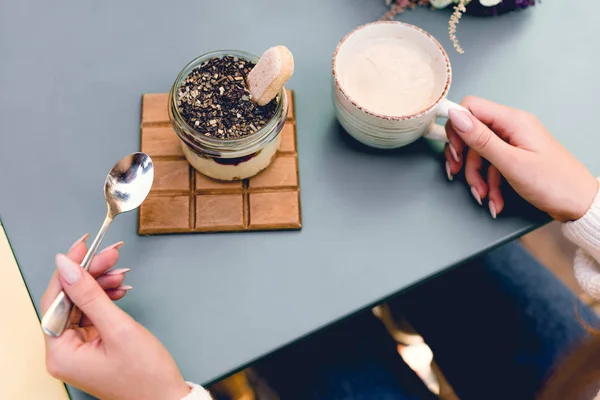 Vue recadrée de la jeune femme tenant cuillère près de dessert savoureux et tasse de café — Photo de stock