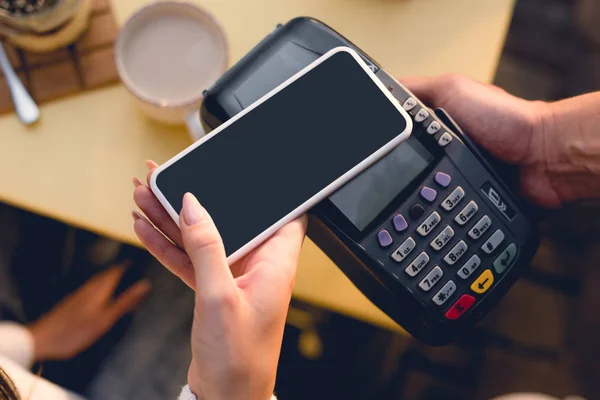 Vista recortada de la mujer joven que paga con teléfono inteligente en la cafetería - foto de stock