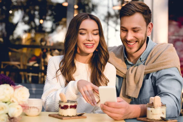 Веселый мужчина сидит с счастливой девушкой указывая пальцем на смартфон — стоковое фото