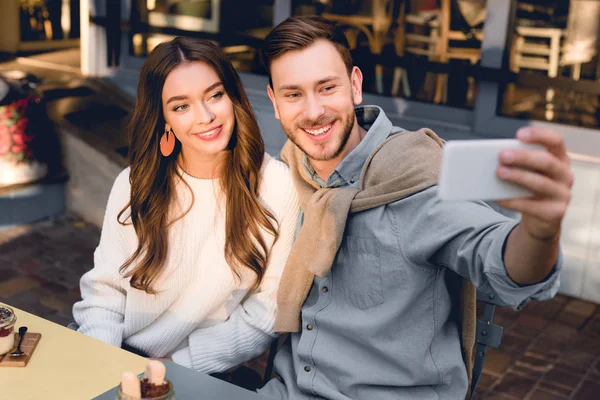 Enfoque selectivo de hombre guapo tomando selfie con chica alegre - foto de stock