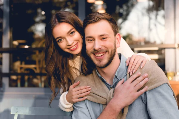 Cheerful girl hugging handsome boyfriend and looking at camera — Stock Photo