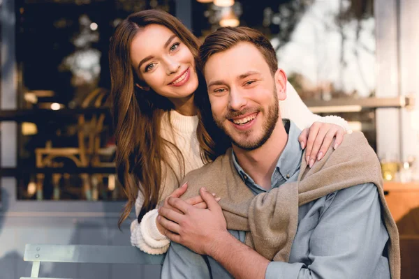 Happy girl hugging handsome boyfriend and looking at camera — Stock Photo