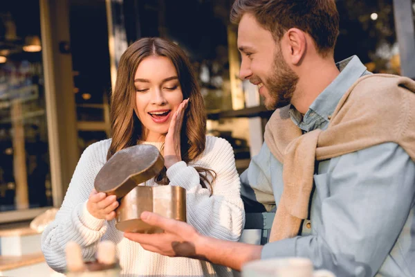 Surprised woman looking at heart-shape box in hand of boyfriend — Stock Photo