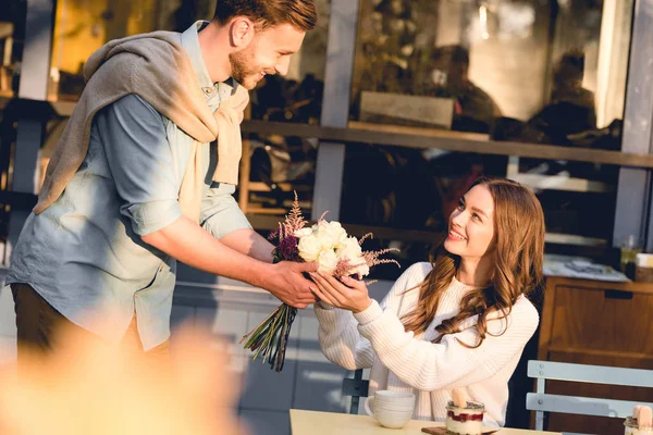 Handsome boyfriend giving bouquet of flowers to cheerful girl — Stock Photo