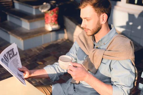 Schöner Mann liest Reisezeitung, während er Tasse hält — Stockfoto