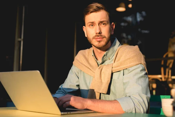 Beau pigiste barbu en utilisant un ordinateur portable tout en travaillant dans un café — Photo de stock