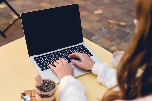 Vista recortada de la mujer joven escribiendo en el ordenador portátil con pantalla en blanco cerca de postre dulce - foto de stock