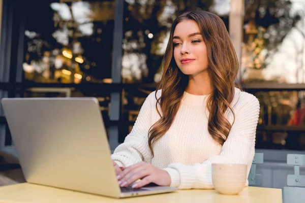 Attractive and happy freelancer using laptop while working in cafe — Stock Photo