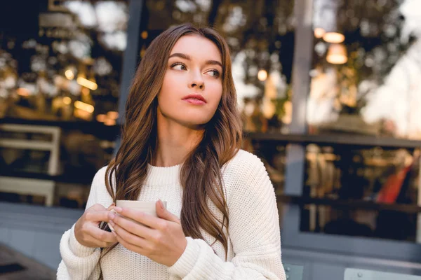 Atractiva mujer joven sosteniendo la taza de café en la cafetería - foto de stock