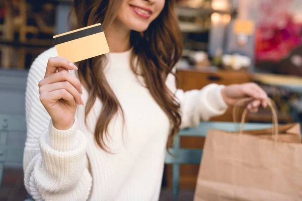 Vista recortada de la niña feliz sosteniendo la tarjeta de crédito y bolsas de compras - foto de stock