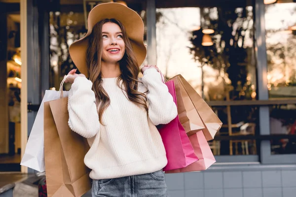 Счастливая молодая женщина в шляпе улыбается, держа сумки — стоковое фото