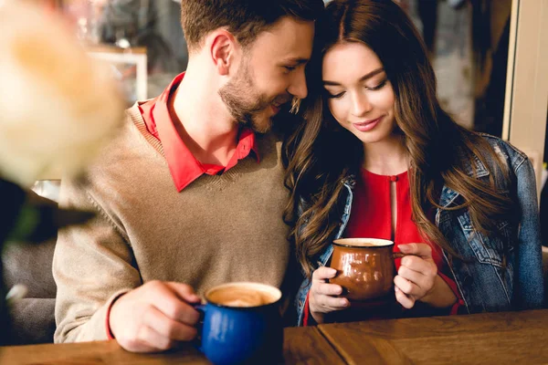 Heureux barbu homme regardant attrayant petite amie tout en tenant tasse de café — Photo de stock