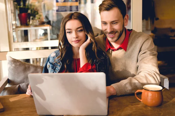 Веселий чоловік і приваблива молода жінка дивиться на ноутбук в кафе — стокове фото