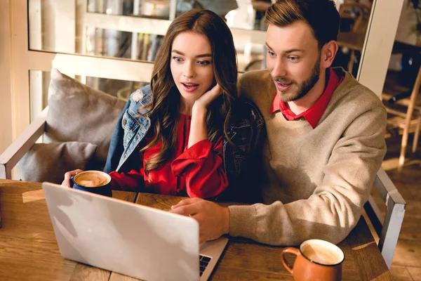 Sorprendido hombre y hermosa mujer joven mirando portátil en la cafetería - foto de stock