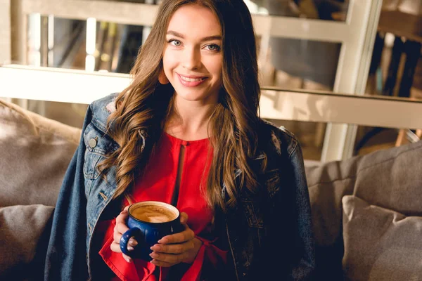 Joyeuse jeune femme tenant une tasse de café et souriant dans le café — Photo de stock