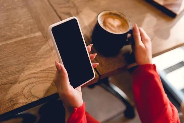 Обрезанный вид женщины, держащей смартфон с пустым экраном возле чашки кофе — стоковое фото