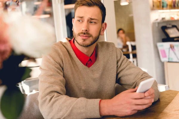 Handsome bearded man holding smartphone in cafe — Stock Photo