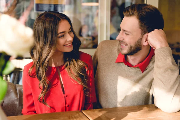 Schöner bärtiger Mann lächelt, während er das schöne Mädchen im Café ansieht — Stockfoto